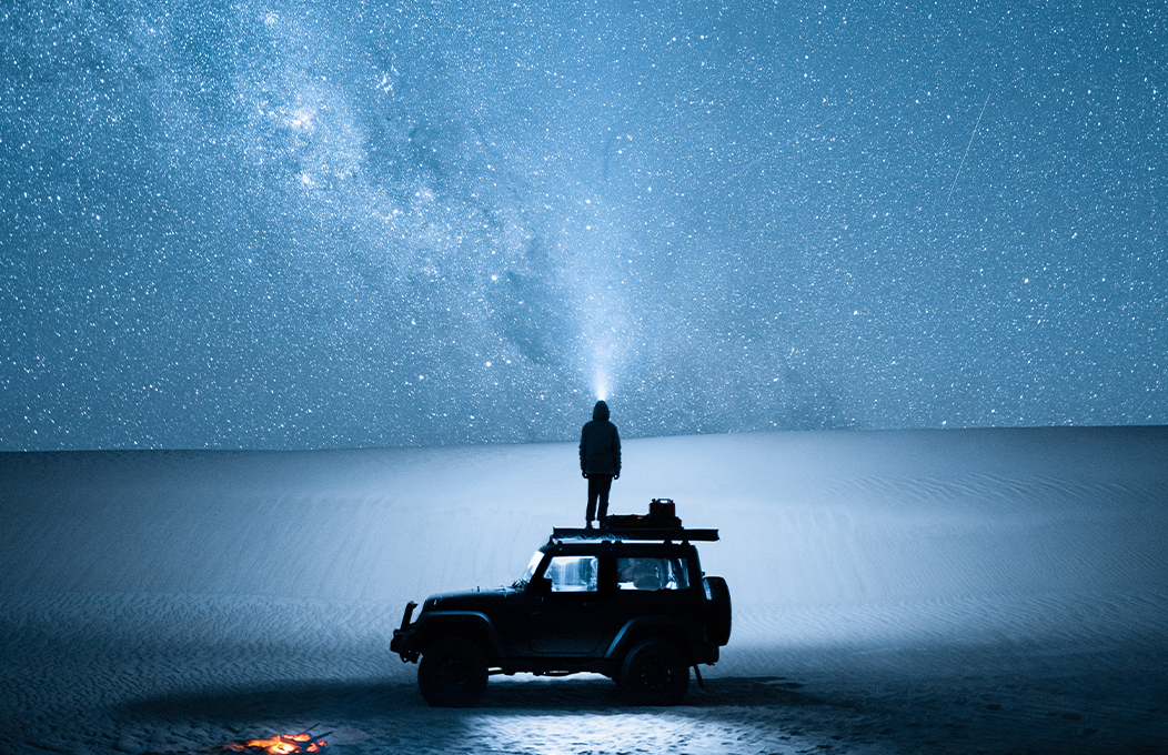 A gentleman staring into the darkness guided only by the torch on his head, and standing on top of his car in an effort to take in more of the views.