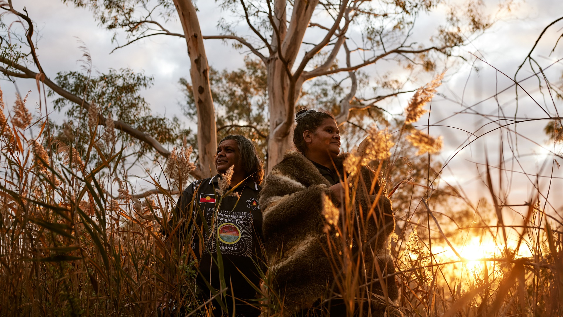 two Aboriginal tour guides standing in the Ngaut Ngaut Conservation Park with the sun setting in the background