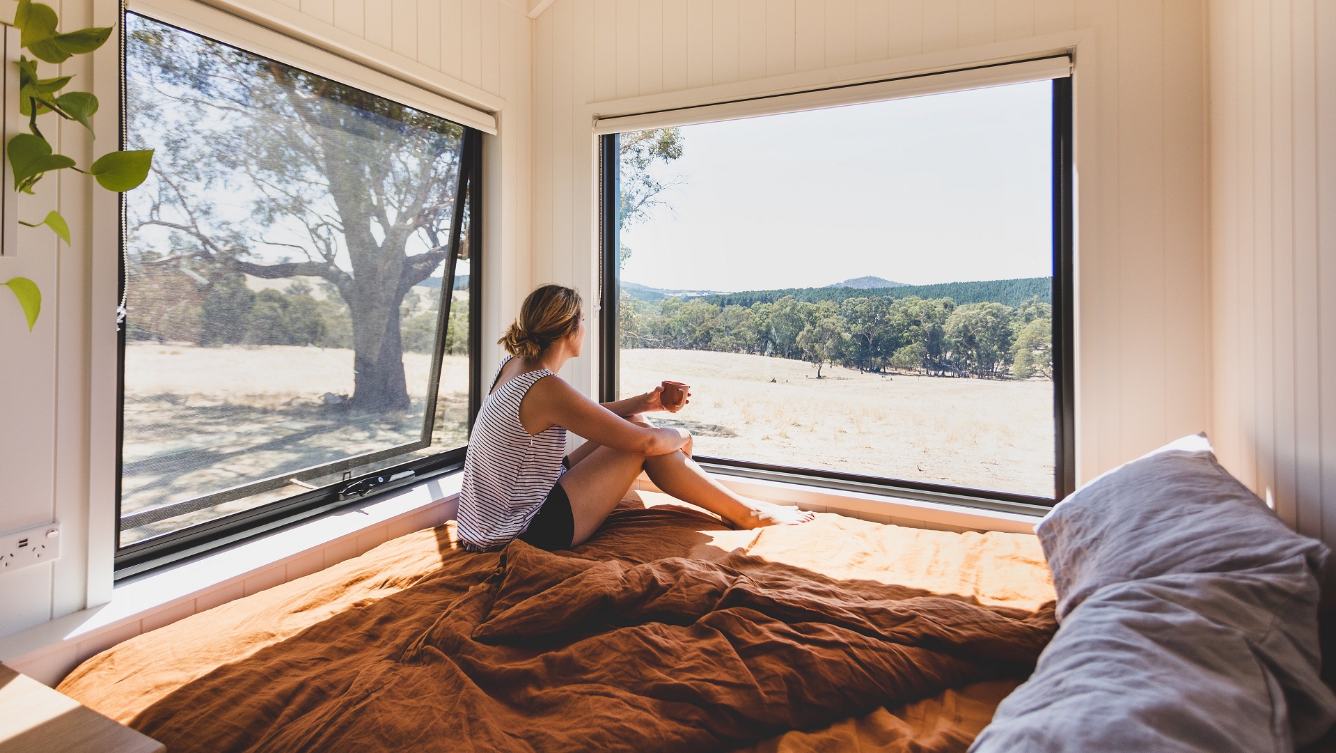 woman sitting on a bed in a tiny home looking out the window and enjoying the beautiful view of the Barossa Valley