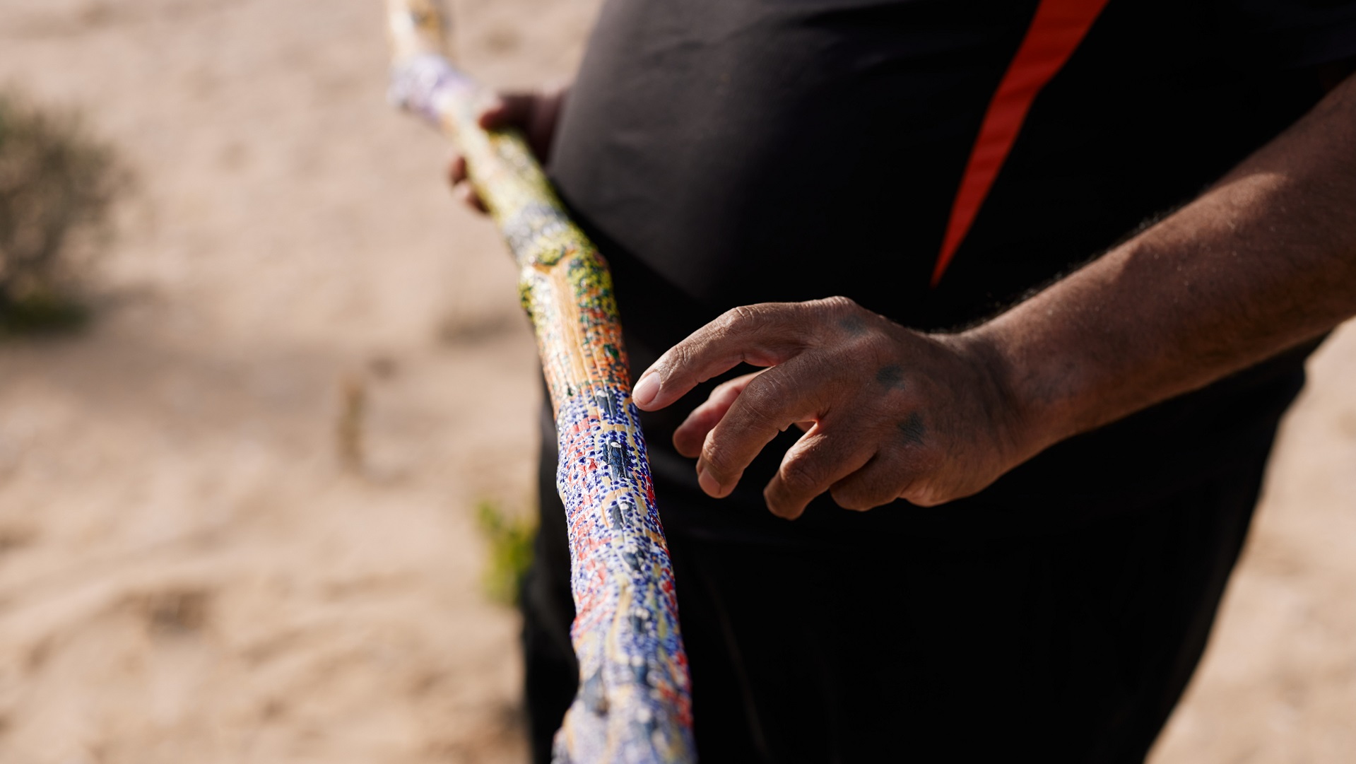 an Aboriginal tour guide holds a painted piece of wood